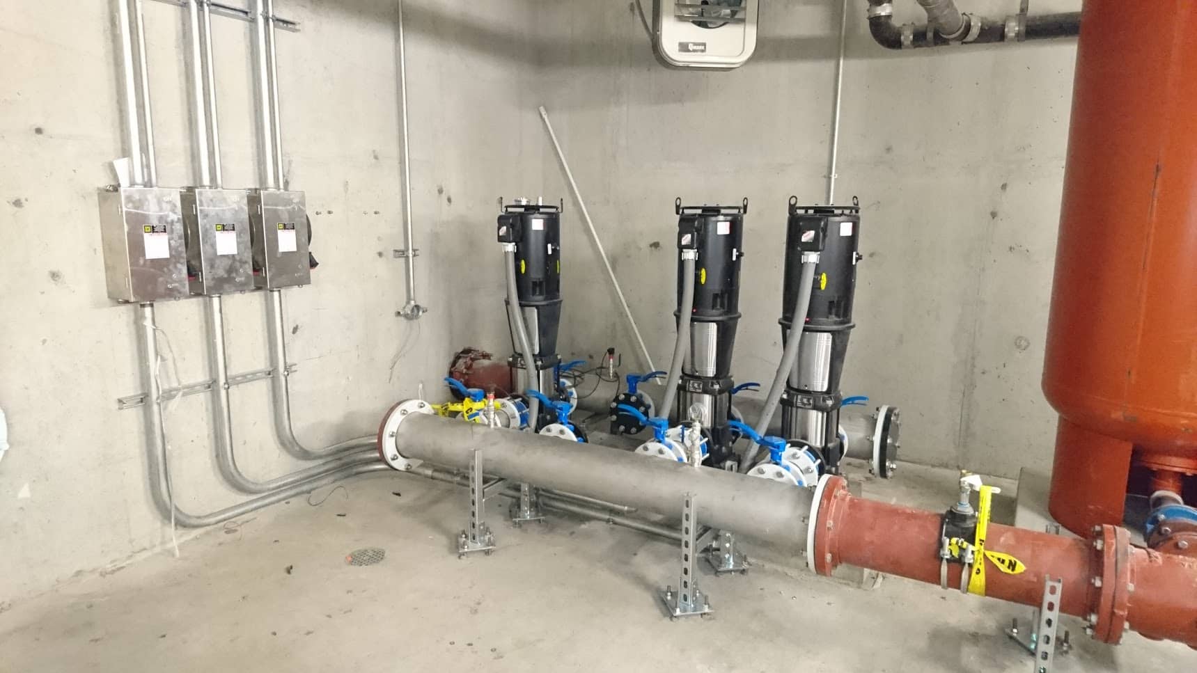 Large pipe and three electrical boxes installed inside concrete room