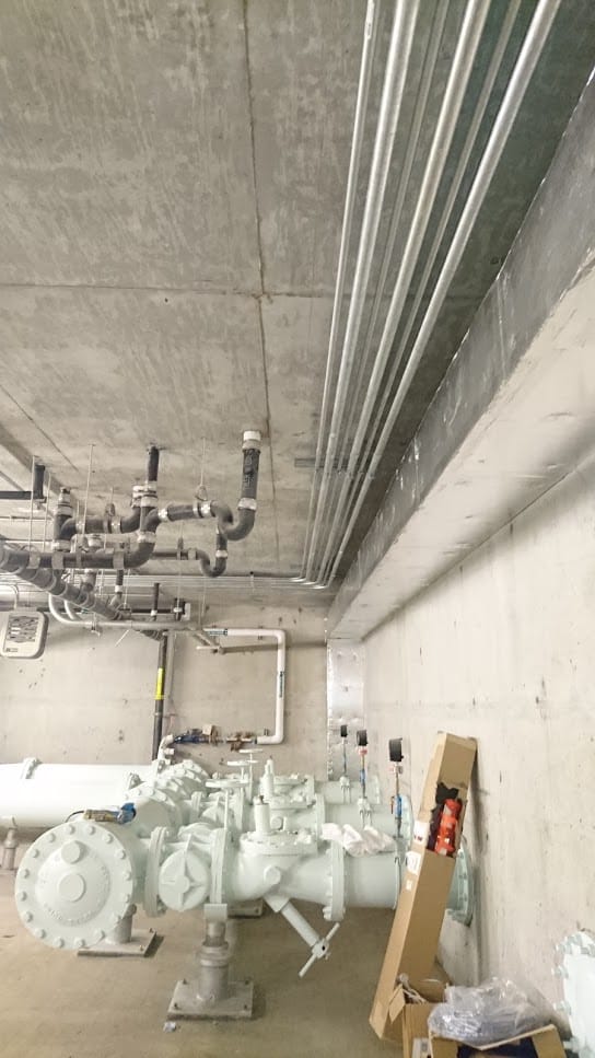 concrete room with small pipes installed on ceiling and large pipes on the floor