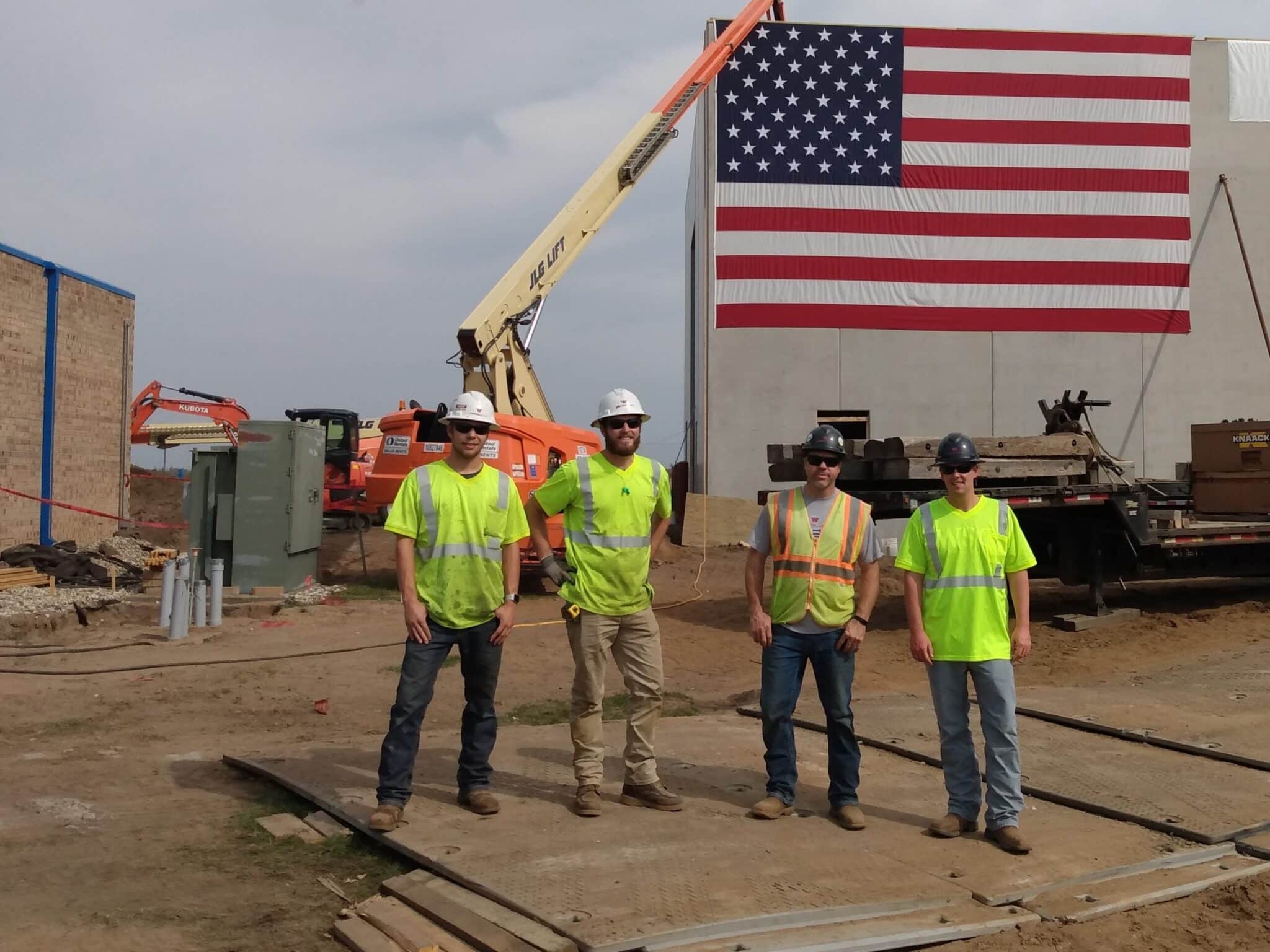 four wescom employees standing at job site in front of crane with 50 foot American flag