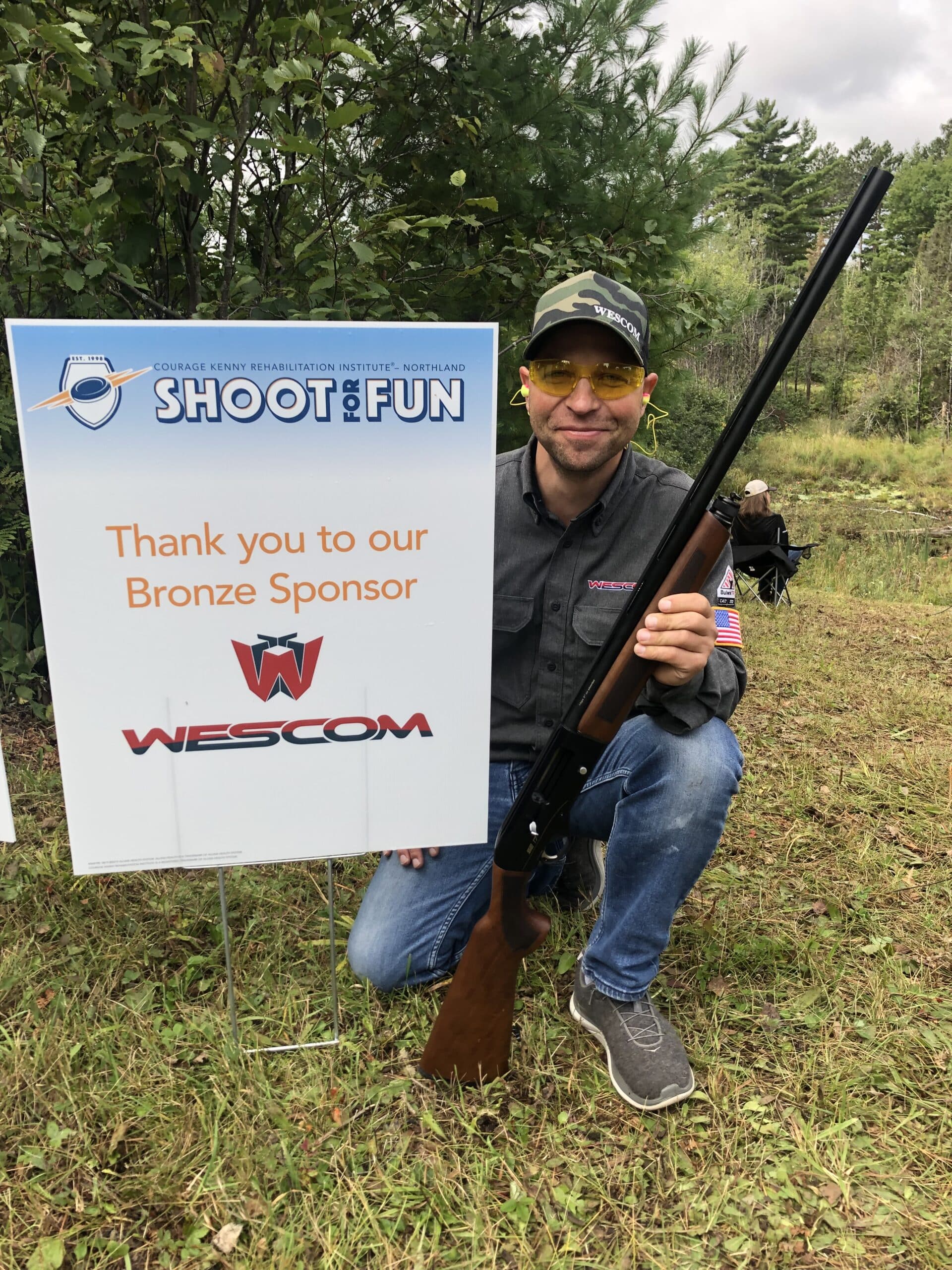 Man with hunting gun posing with a sign reading 'thank you to our bronze sponsor, wescom'