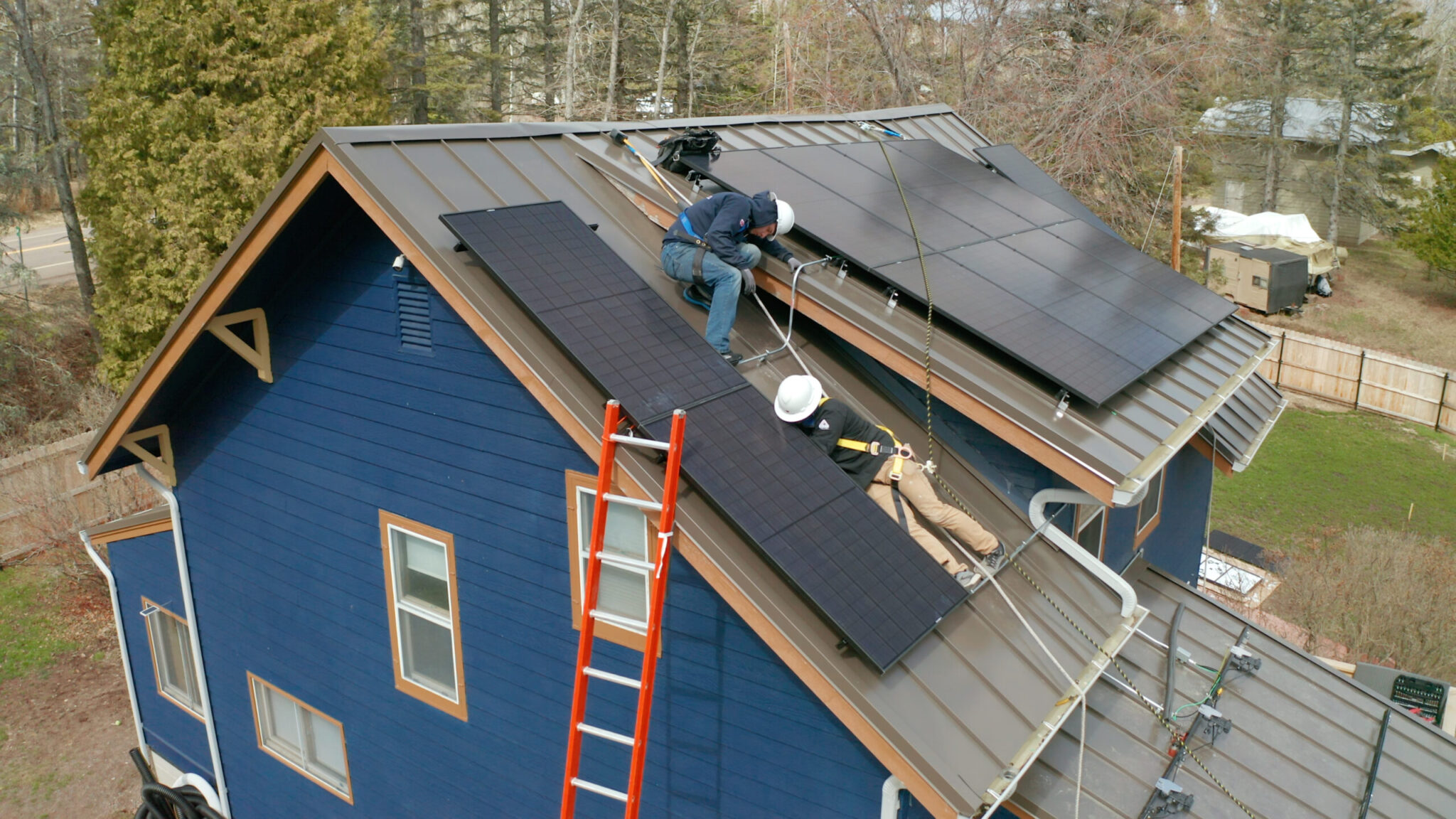 Two men installing wescom solar panels on a blue house. The family who owns the house will receive solar energy savings.