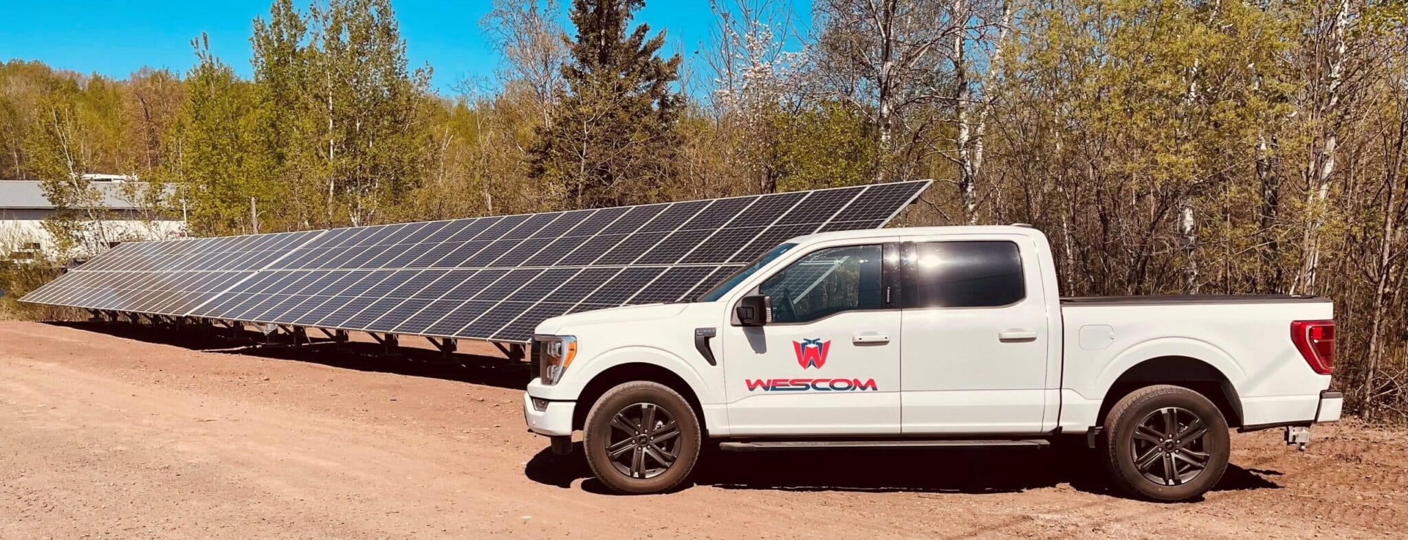 Wescom truck parked outside of a row of solar panels and trees behind