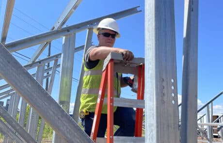 A man in safety vest and hard hat on a ladder while on a job site.