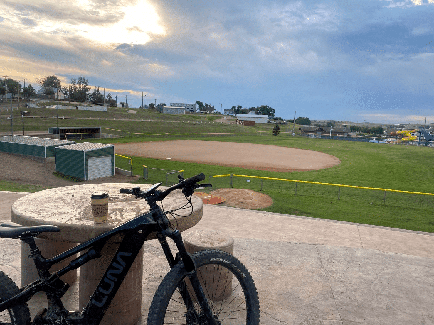 Bike and a to-go coffee at a table overlooking a baseball field