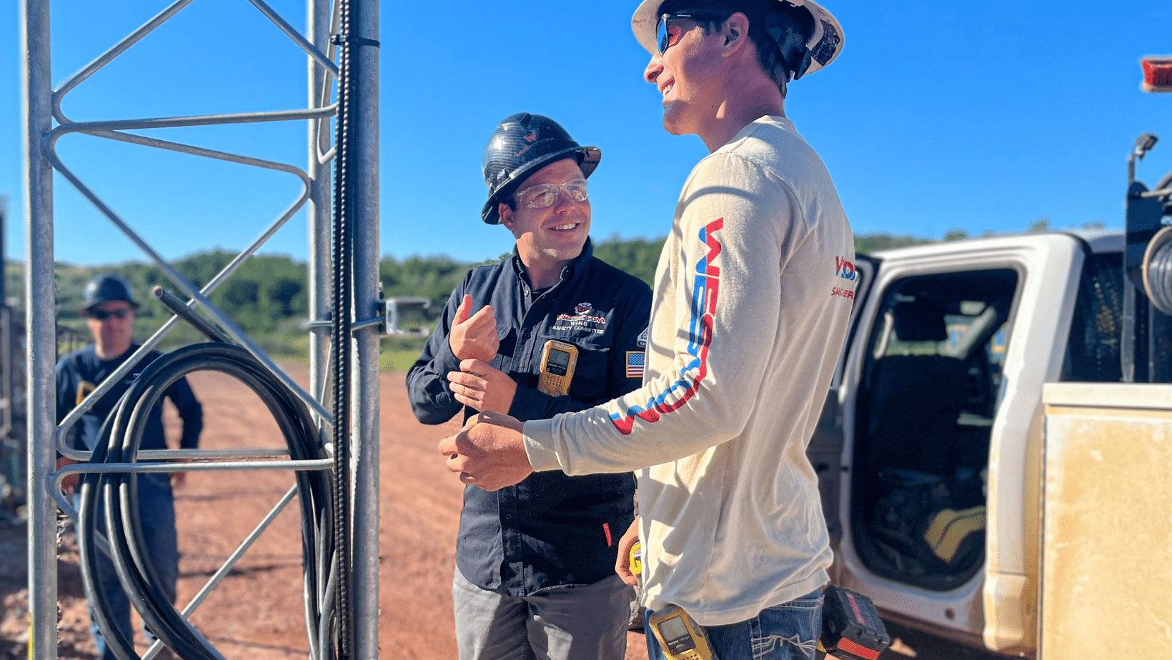Shane Stolp smiling at a field worker at a job site in the Bakken. Two men wearing wescom apparel smiling outside while working.