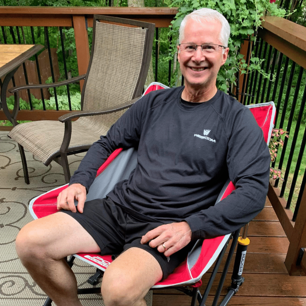 Smiling older gentleman in red camping chair and decked out in Wescom clothing which he won at the event