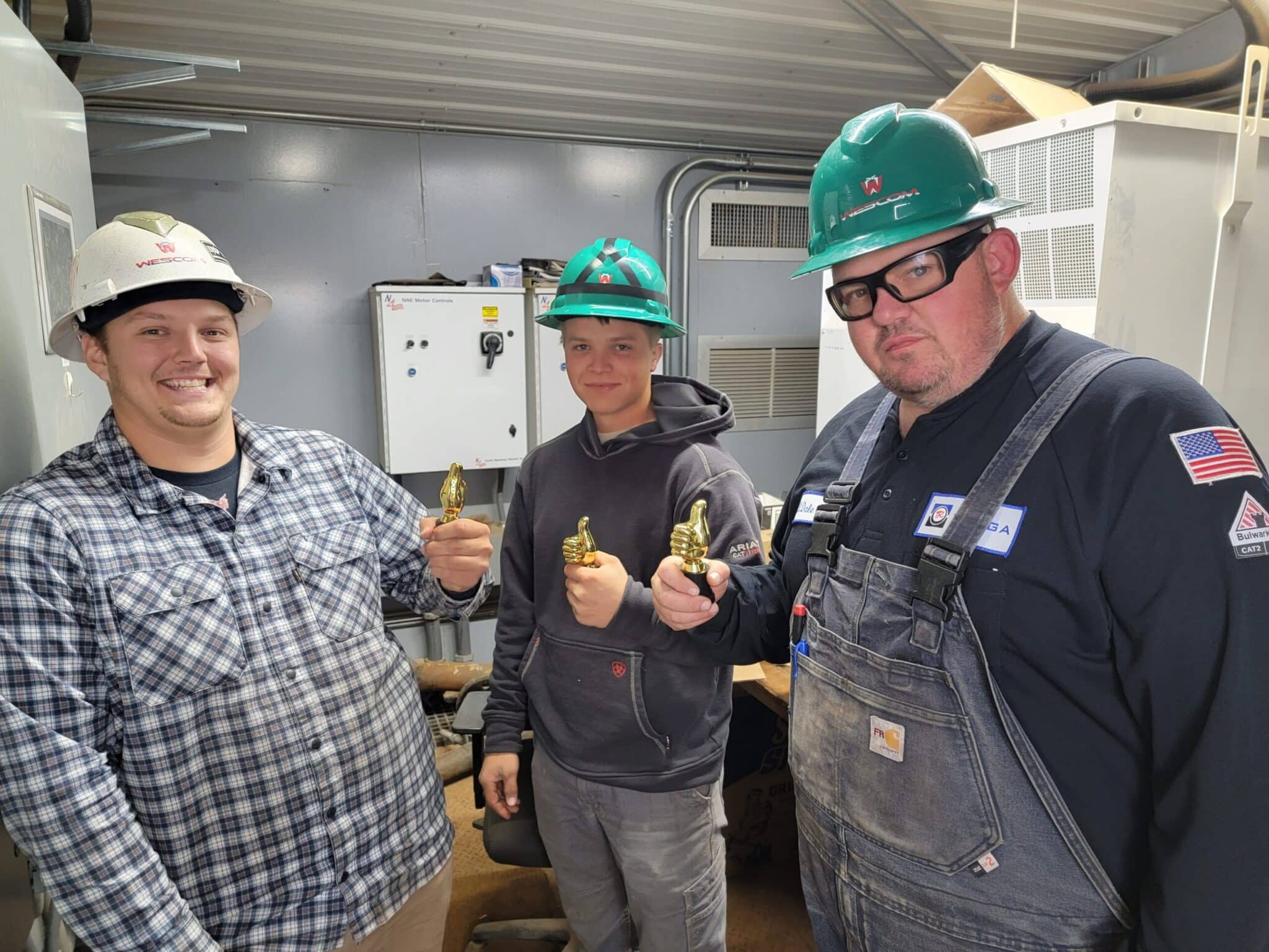 For values post, three men standing at work while wearing wescom apparel and hard hats and holding trophies