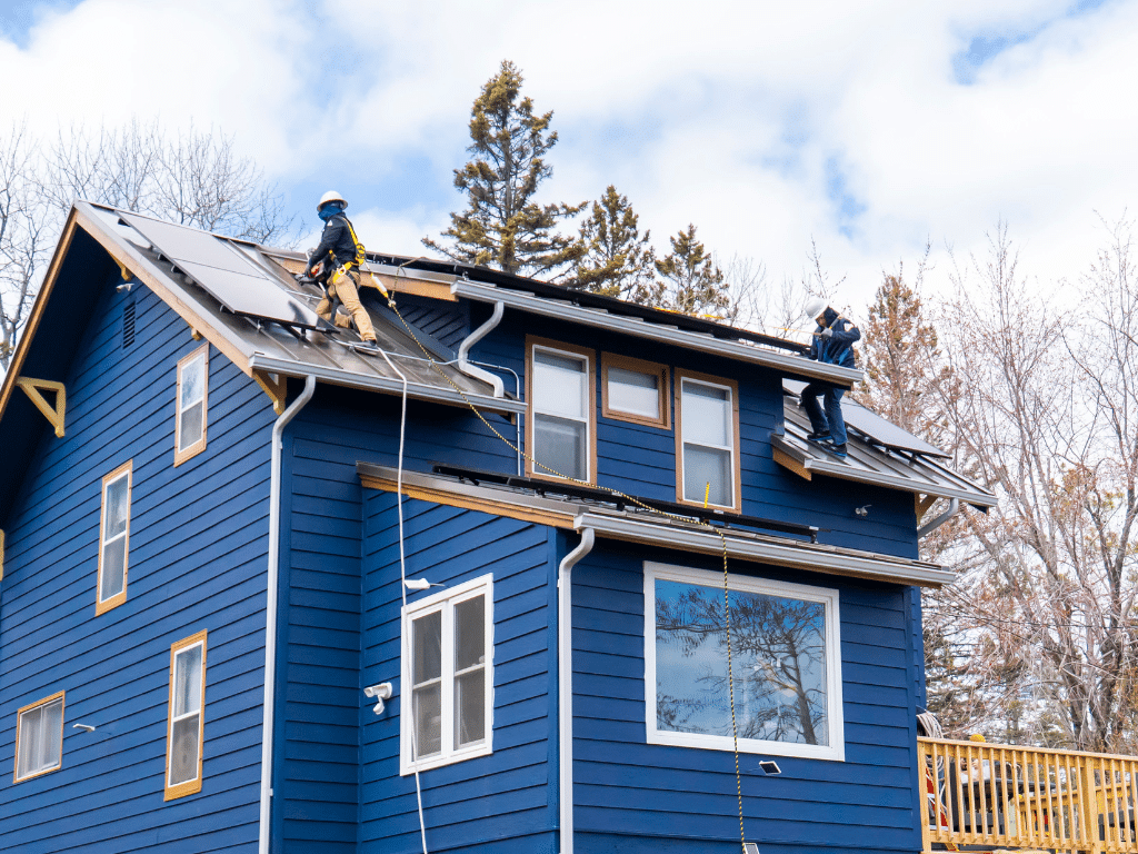 Solar Installation on the roof of a blue house. Two men are safely hooked up to take care of the installation.