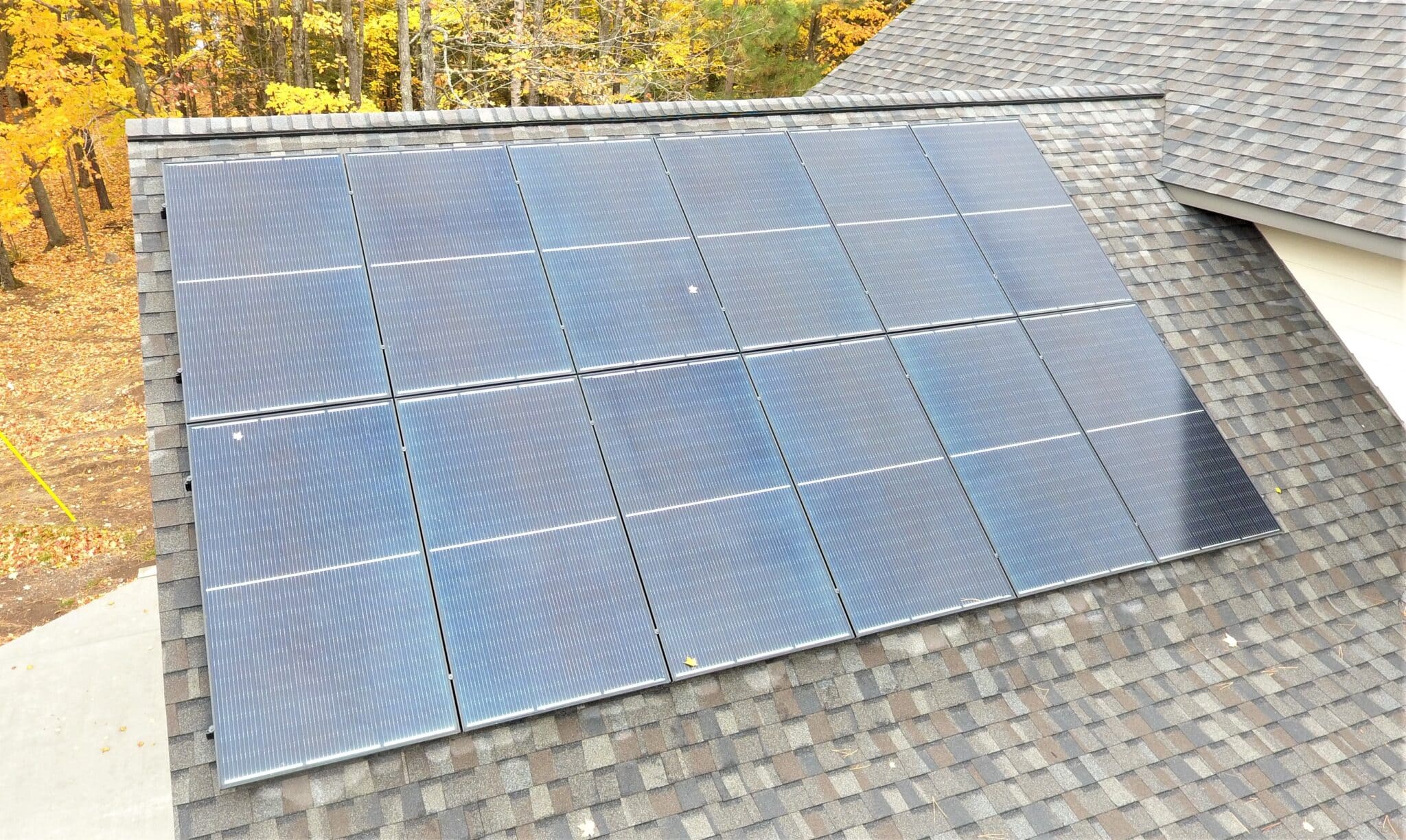 An aerial shot of rows of roof-mounted solar with trees in the background.
